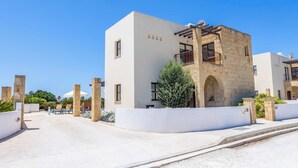 A modern building with a stone facade, a balcony, and a pool area with lounge chairs. - Villa Anthia (Pegeia)