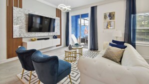 A modern living room with a flat-screen TV, a marble accent wall, a sofa, two blue chairs, and a patterned rug.