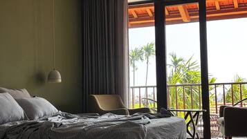 Een slaapkamer met een groot bed, een stoel, een balkon met uitzicht op palmbomen en een plafondventilator.