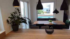 A modern dining area with a wooden table, black pendant lights, and a potted plant. - Villa With Panoramic Views on the Sea, Islands, City and Hill (Kaštel Sućurac)