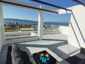 A rooftop terrace with a glass balustrade, a black coffee table with drinks, and a view of the sea and distant buildings. - Villa With Panoramic Views on the Sea, Islands, City and Hill (Kaštel Sućurac)