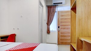 Habitación de hotel con cama, escritorio, armario y ventana con cortinas.