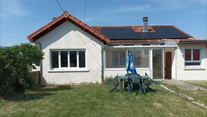 Una casa con fachada blanca, techo de tejas rojas y un panel solar.