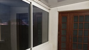 Una habitación con un amplio ventanal corredero, una puerta de madera con paneles de vidrio y suelo de baldosas.