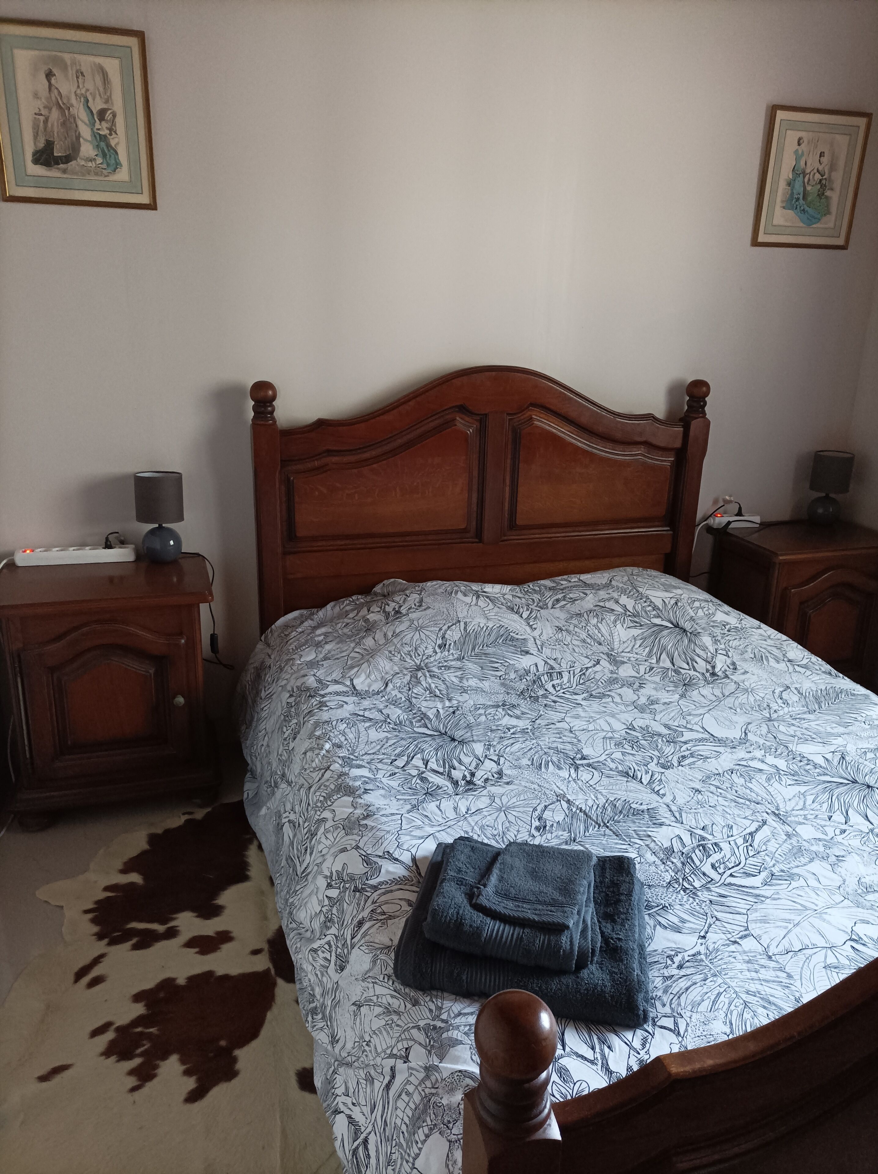 Un dormitorio con una cama de madera, una colcha estampada, un tapiz de cuero de vaca y dos mesitas de noche con lámparas.