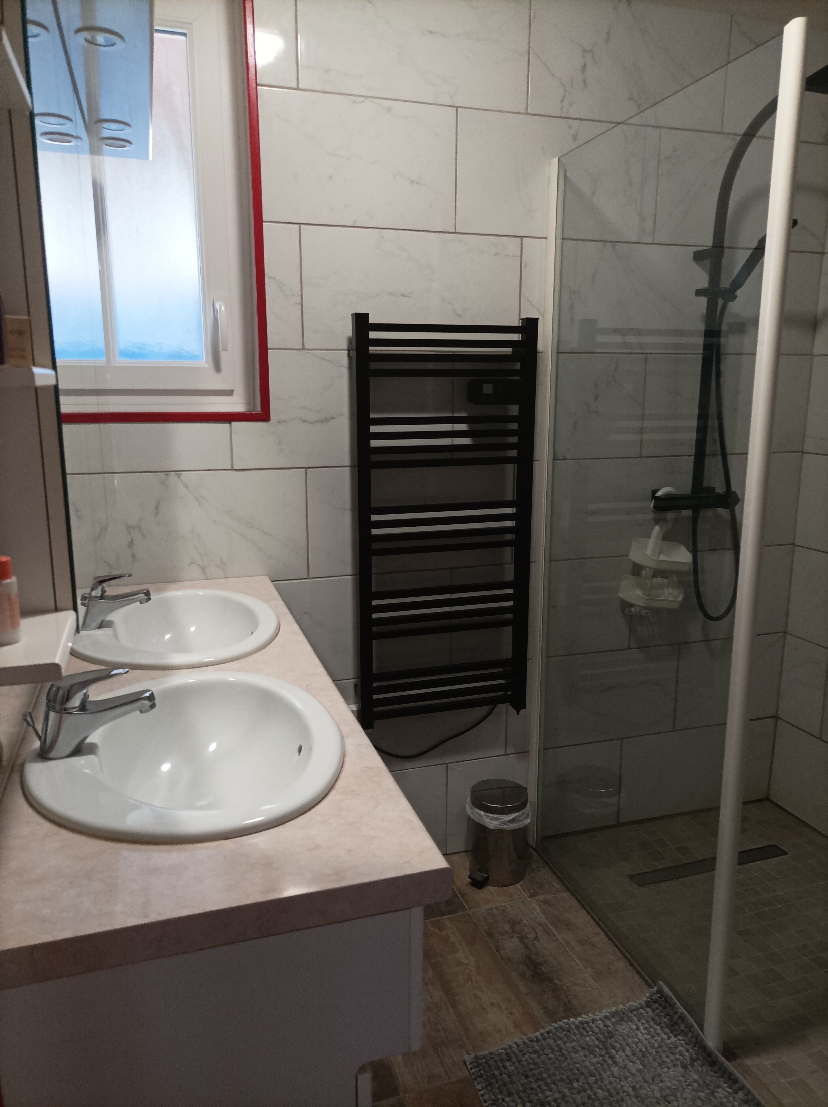 Een badkamer met twee wastafels, een douchecabine van glas en een handdoekrek.