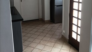 Un pasillo con suelo de baldosas, una puerta, un refrigerador y una ventana con persianas.