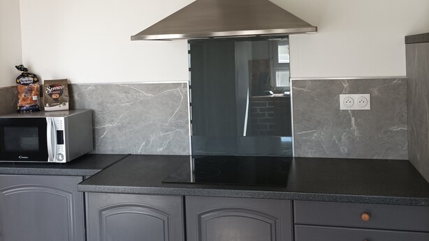 Una cocina con extractor de acero inoxidable, microondas y tostadora. Hay armarios con cajones y una encimera.