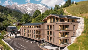 Un hotel de varios pisos con estacionamiento, rodeado de montañas y vegetación.