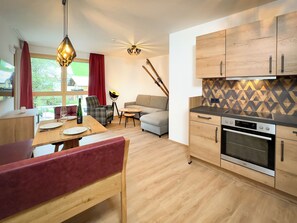 A modern kitchen with wooden cabinets, a built-in oven, and a dining area with a table and chairs. - AlpenParks Wildbach Lodge Hochkönig (Dienten am Hochkoenig)