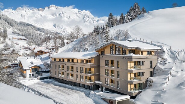 Un hotel de varios pisos con un diseño moderno, situado en una zona montañosa nevada con cielos despejados.