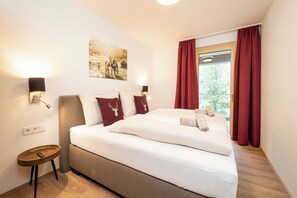 Ein Hotelzimmer mit einem großen Bett, einem Nachttisch mit Lampe, einem Bild an der Wand und einem Fenster mit roten Vorhängen.