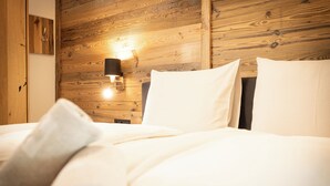 Una cama con sábanas y almohadas blancas, un cabecero de madera y una lámpara fijada a la pared.