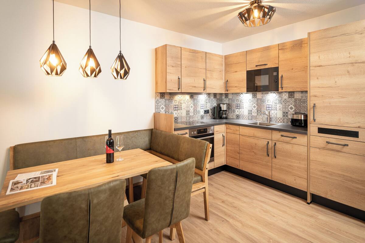 A modern kitchen with wooden cabinets, a dining table with chairs, and pendant lighting.