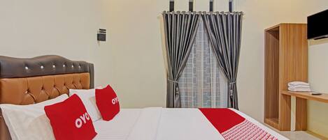 A hotel room with a large bed, a wooden headboard, a TV on a wooden shelf, and a window with curtains.