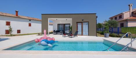 A swimming pool with inflatable toys, a covered patio area, and a building with a modern design.