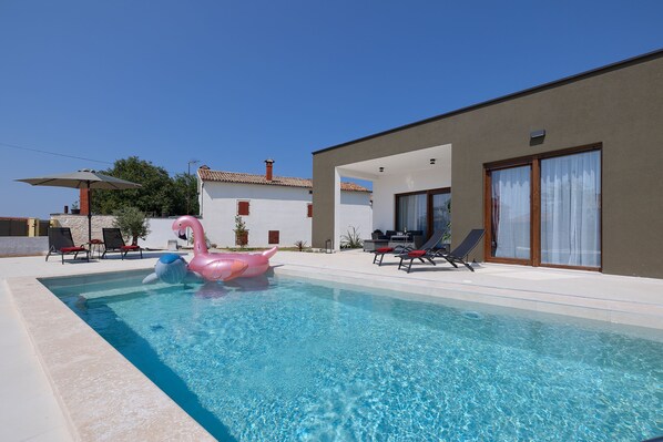 A swimming pool with a pink flamingo float, lounge chairs, and a modern building with large windows. - House Bronzin by Istra Vacation (Kanfanar)