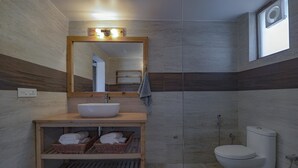 Un baño moderno con tocador de madera, un espejo grande, un lavamanos blanco, un inodoro y una zona de ducha.