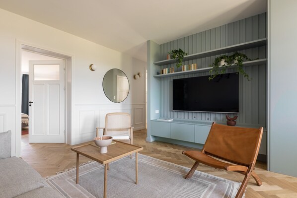 A living room with a TV, a wicker chair, a brown leather chair, and a small table with a bowl.
