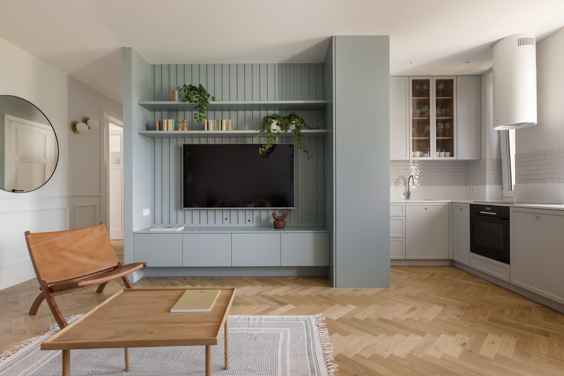 A modern kitchen with built-in appliances, a dining area with a wooden table and bench, and a TV mounted on a light blue wall.