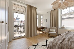 A bedroom with a large window, a desk, a chair, and a bed.