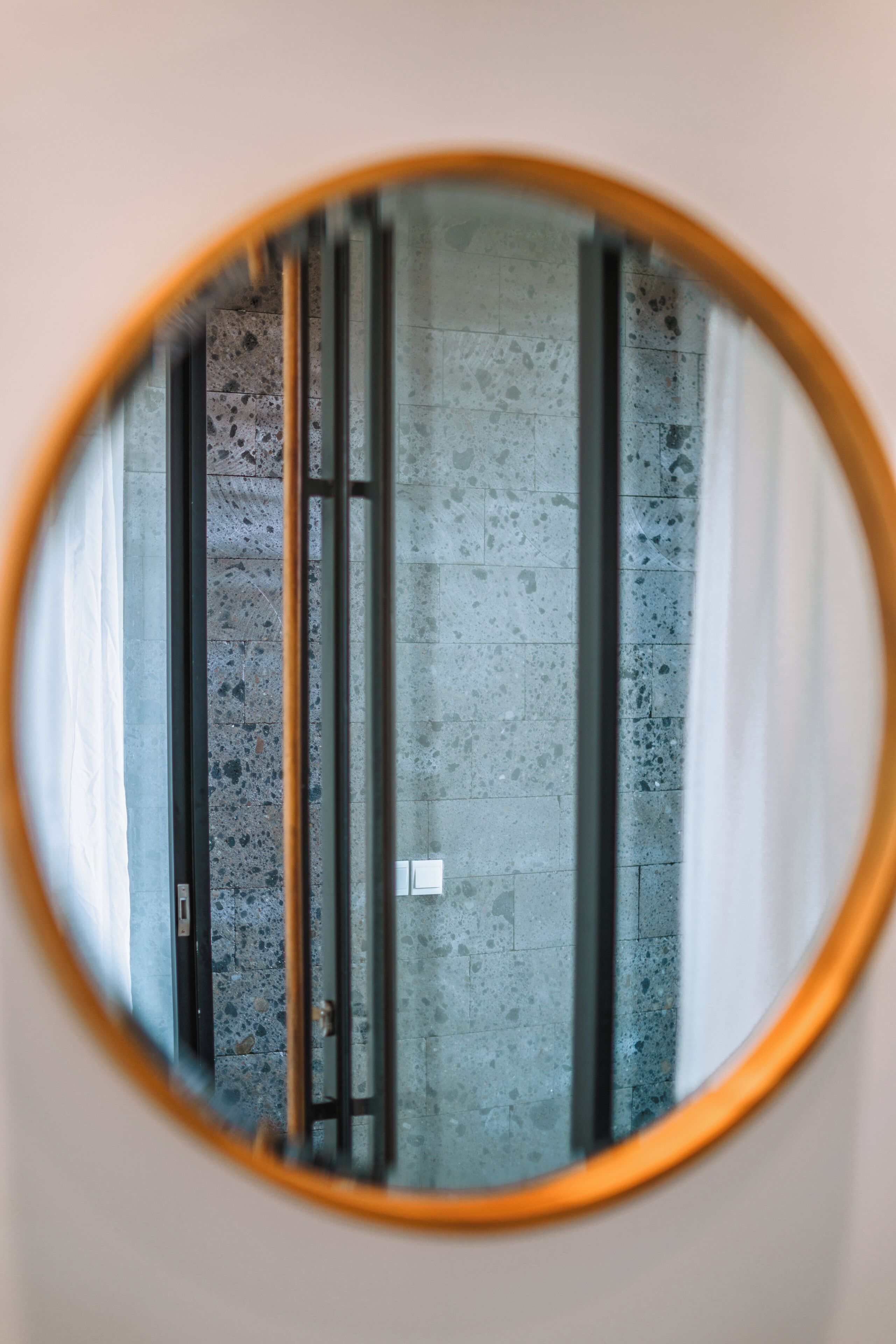 A round mirror with a wooden frame reflecting a tiled floor and a door.