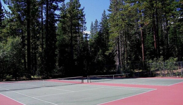 Una cancha de tenis al aire libre rodeada de árboles altos.