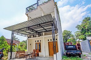 A two-story house with a covered patio, a wooden door, and a black pickup truck parked outside. - Hotel O Omahku Hostel Bunkbed (Yogyakarta)