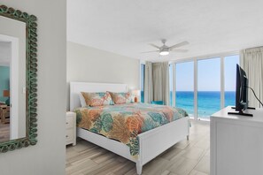 A bedroom with a bed, a television, a ceiling fan, and a view of the ocean.