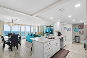 A modern kitchen with a large island, dining area with a view, and a living room with a sofa and a view.