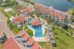Vista aérea de um resort com vários edifícios, uma piscina central e um corpo de água.