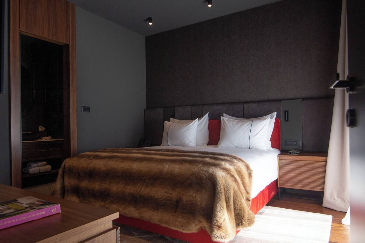 A modern hotel room with a large bed, wooden flooring, and a built-in wardrobe.