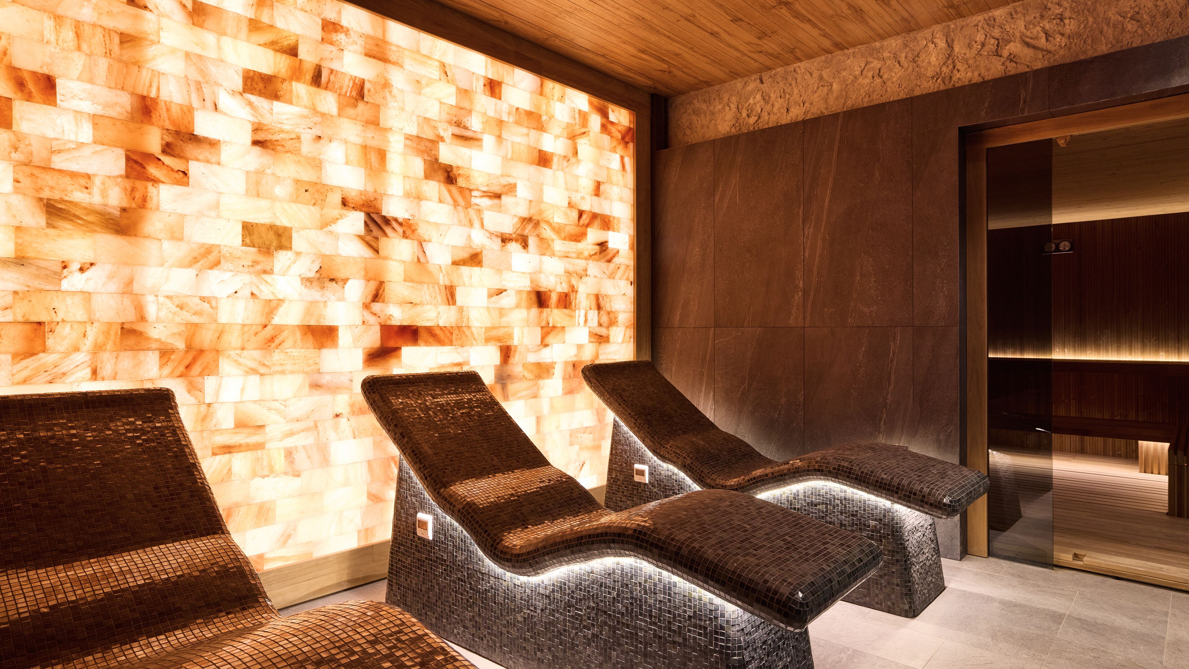Een wellnessruimte met houten wandpanelen en zwarte loungestoelen.