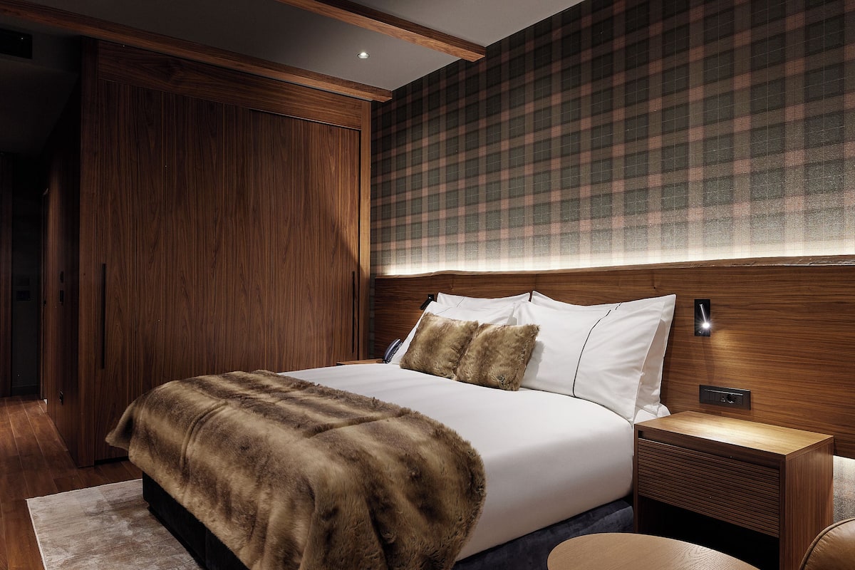 A modern bedroom with a large bed, wooden headboard, and a plaid-patterned wall.