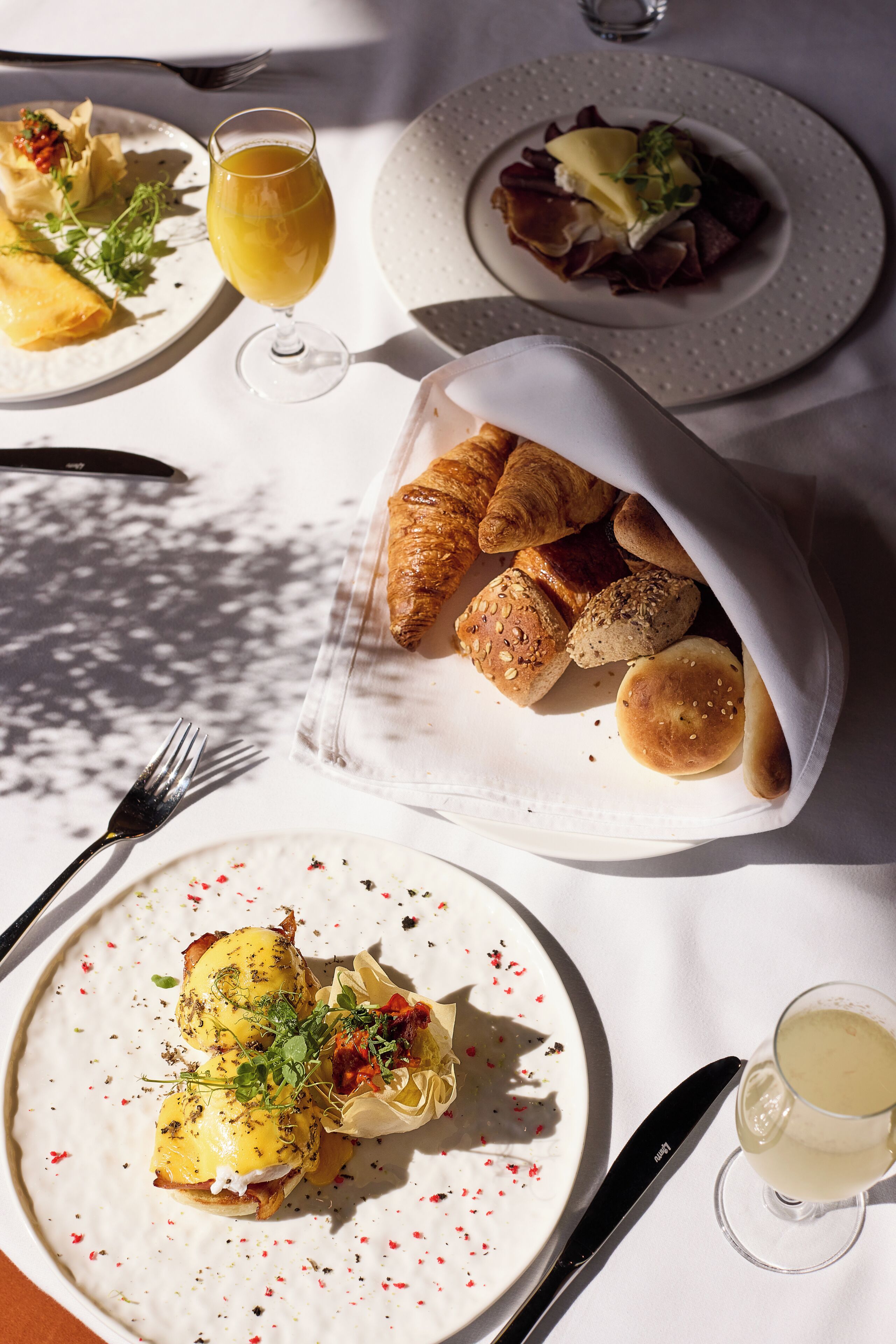 Una mesa dispuesta con diversos platos, incluyendo croissants, una ensalada y un plato de huevos benedictinos.