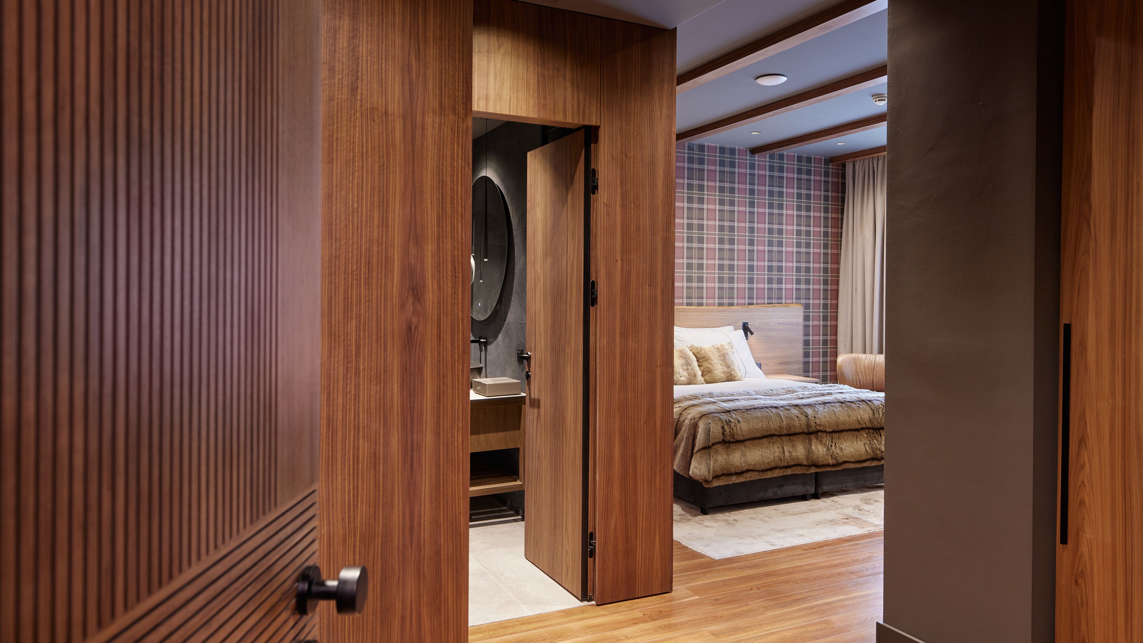 A modern bedroom with a wooden wardrobe, a bed with a headboard, and a tiled wall.