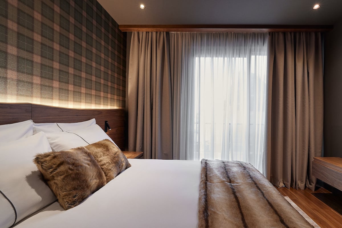 A hotel room with a large bed, a headboard with a checkered pattern, a flat-screen TV, and a large window with curtains.