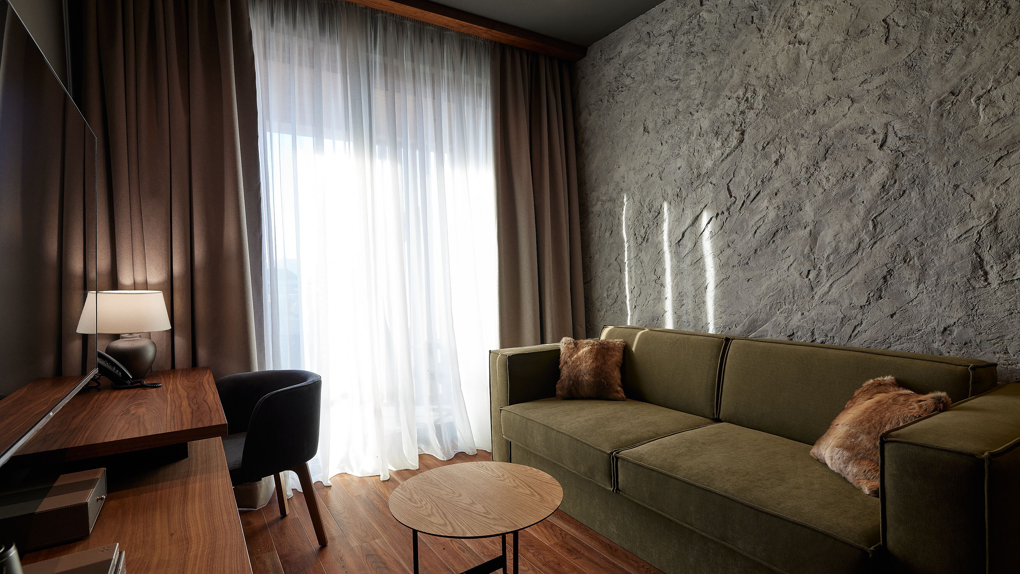 Una sala de estar moderna con un escritorio de madera, un sofá verde y una mesa redonda de madera.