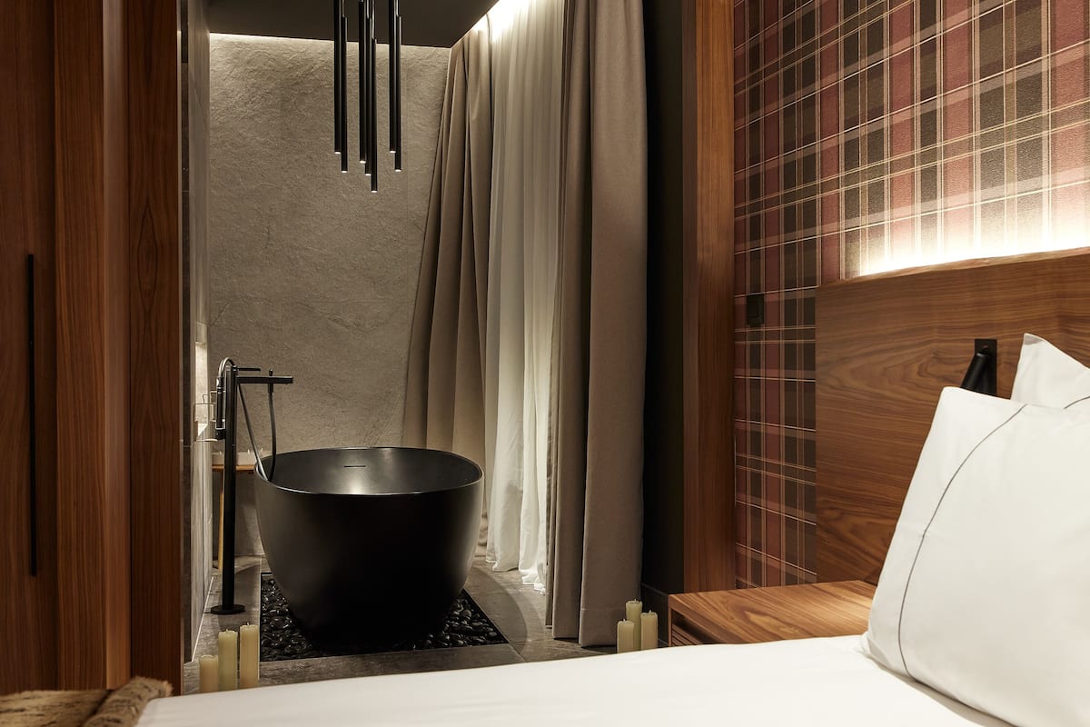 A modern bathroom with a freestanding bathtub, a shower area, and a wooden headboard.