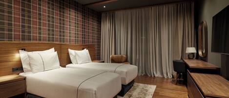 A modern hotel room with two beds, wooden headboards, a large mirror, and a view of the cityscape through floor-to-ceiling windows.