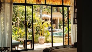 A bedroom with a large window overlooking a pool and garden. - Hani Hideaway (Gili Air)