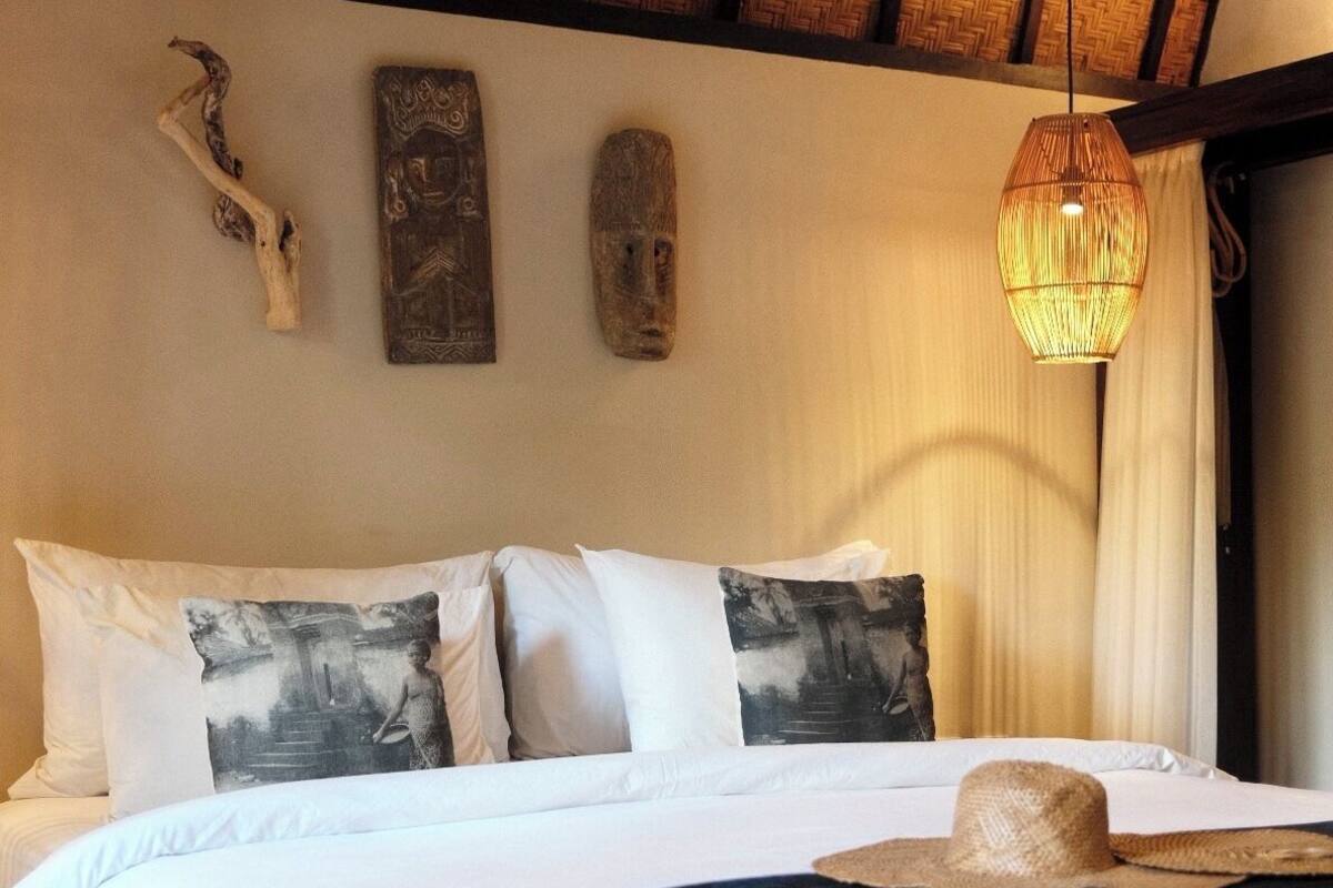 A bedroom with a wooden ceiling, a bed with white bedding, and a woven headboard.