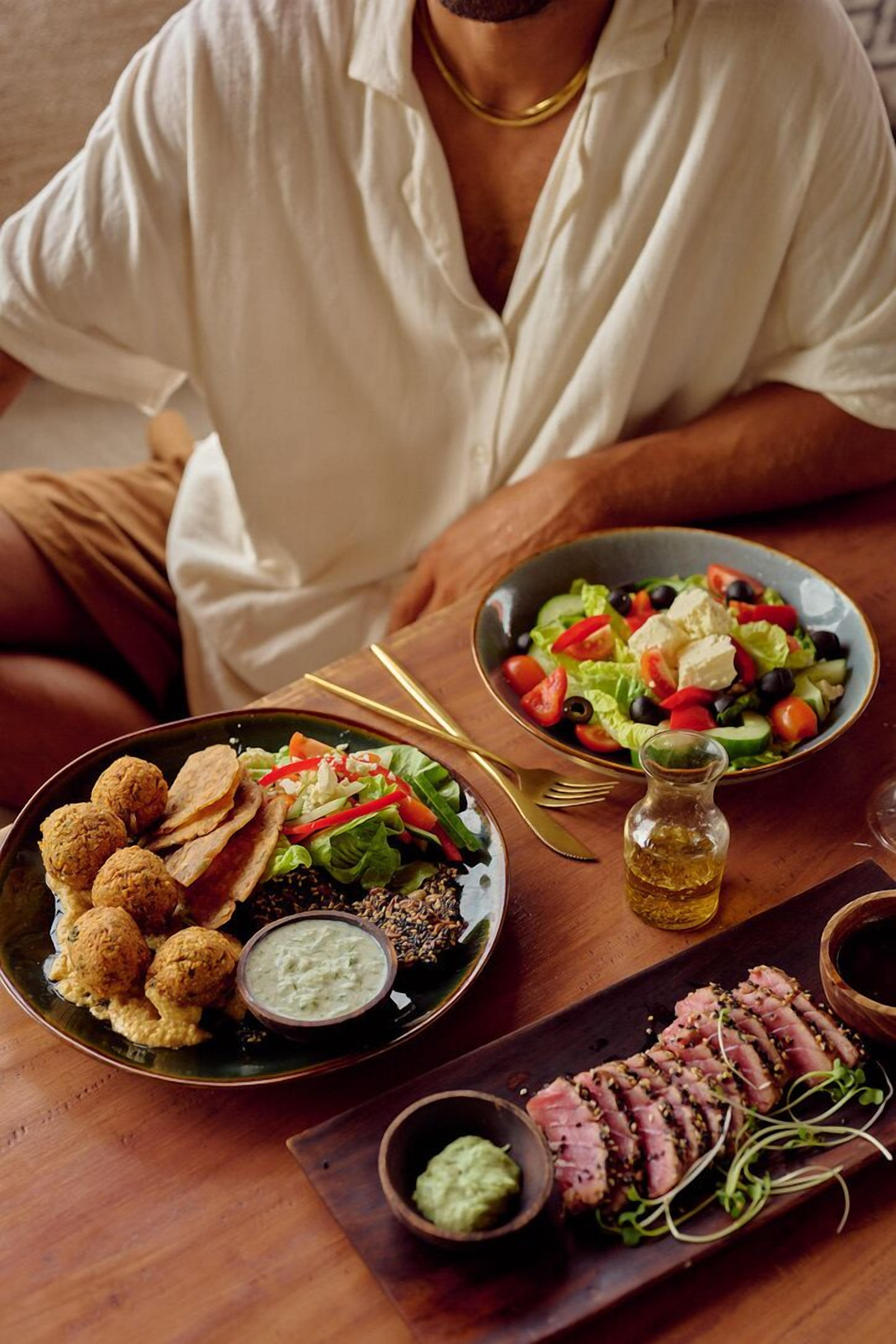 Una mesa de comedor con varios platos, incluyendo falafel, ensalada y carne en rebanadas, acompañados de salsas para mojar.