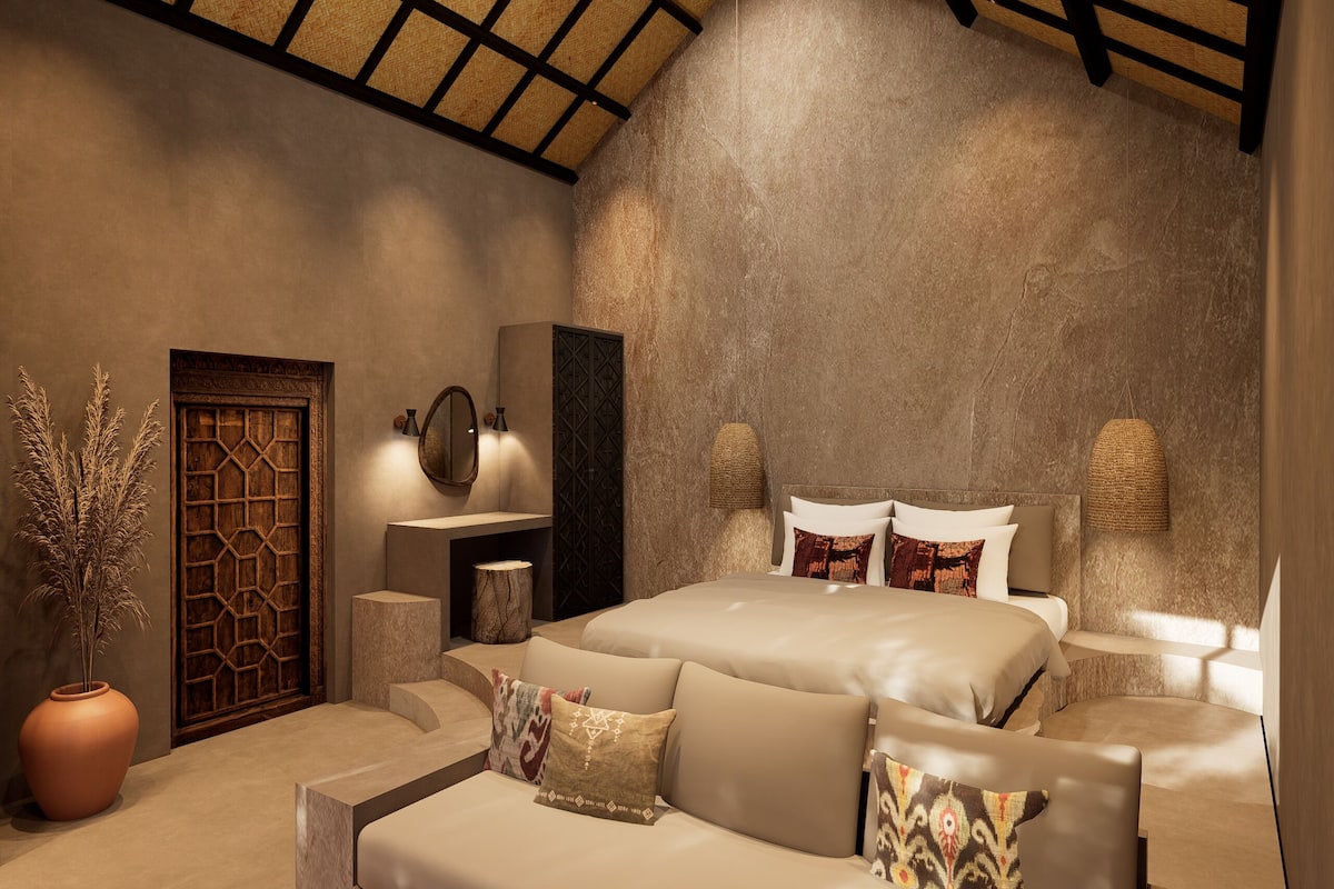 A bedroom with a large bed, a potted plant, a wooden door, and a stone wall.