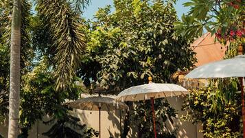 Zona junto a la piscina con una tumbona, una mesita y una sombrilla grande.
