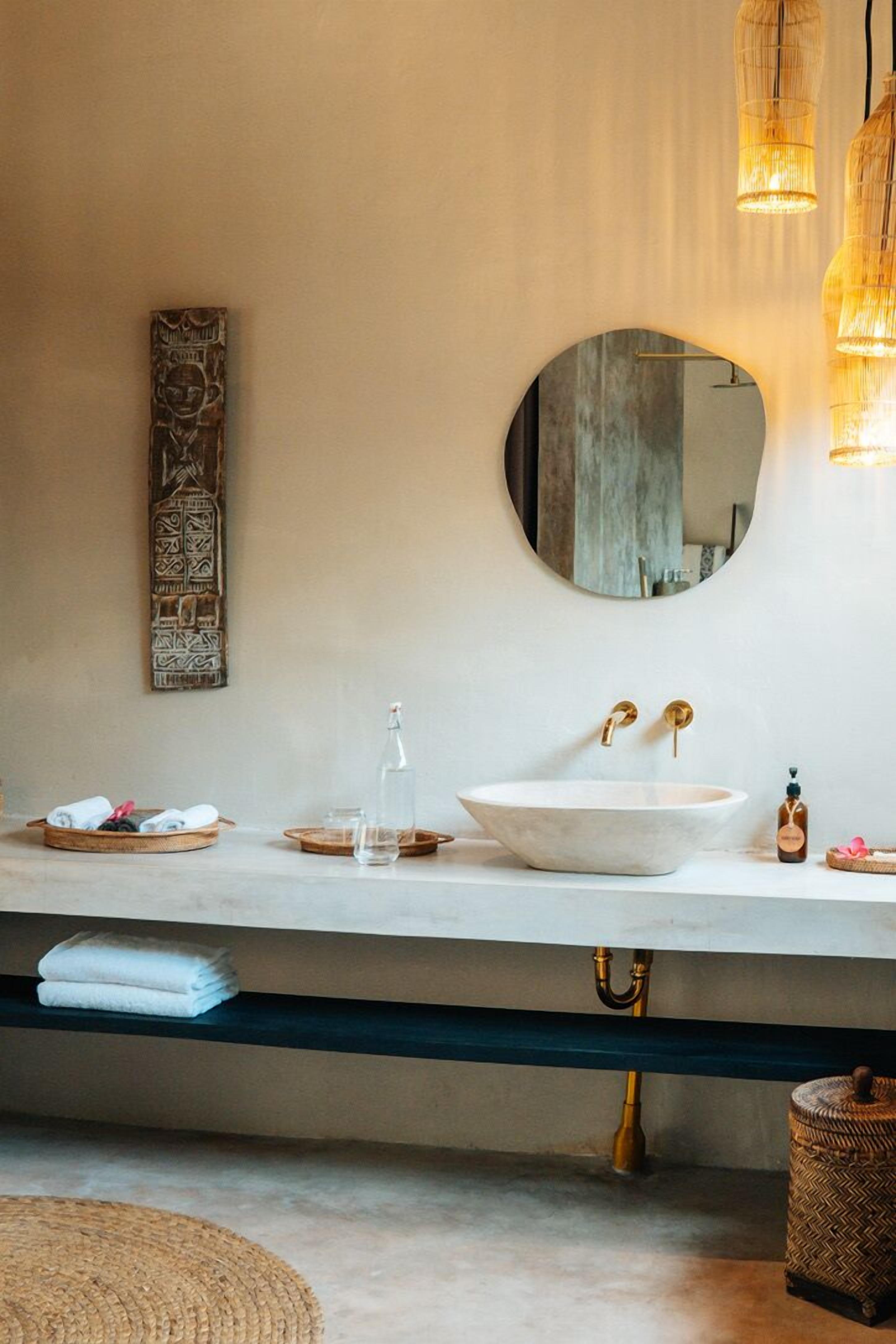 A bathroom with a white sink, gold faucets, a round mirror, and a woven basket.