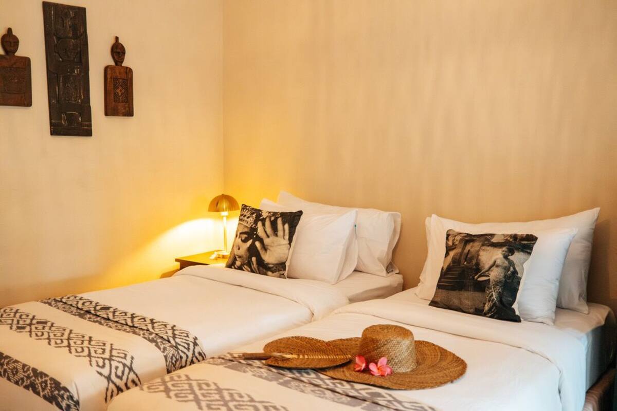 A hotel room with two beds, a lamp, and decorative pillows.