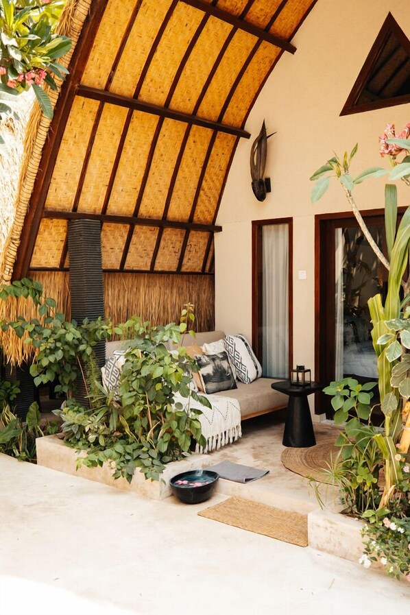 A cozy outdoor seating area with a thatched roof, a cushioned sofa, and potted plants.