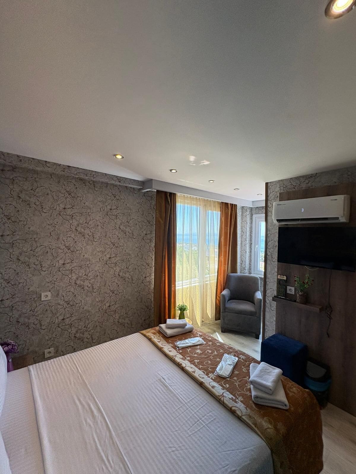 A hotel room with a bed, a chair, an air conditioning unit, and a view through the window.
