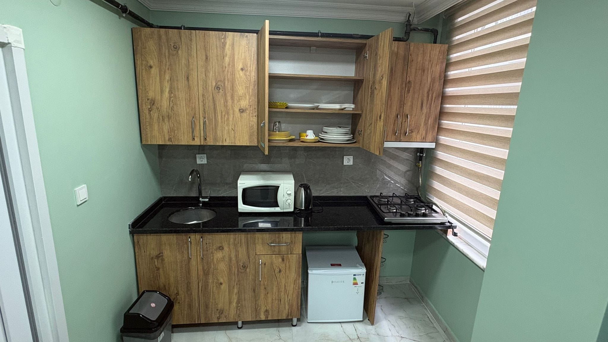 Una cucina compatta con mobili in legno, un lavello, un forno a microonde, un fornello e un piccolo frigorifero.